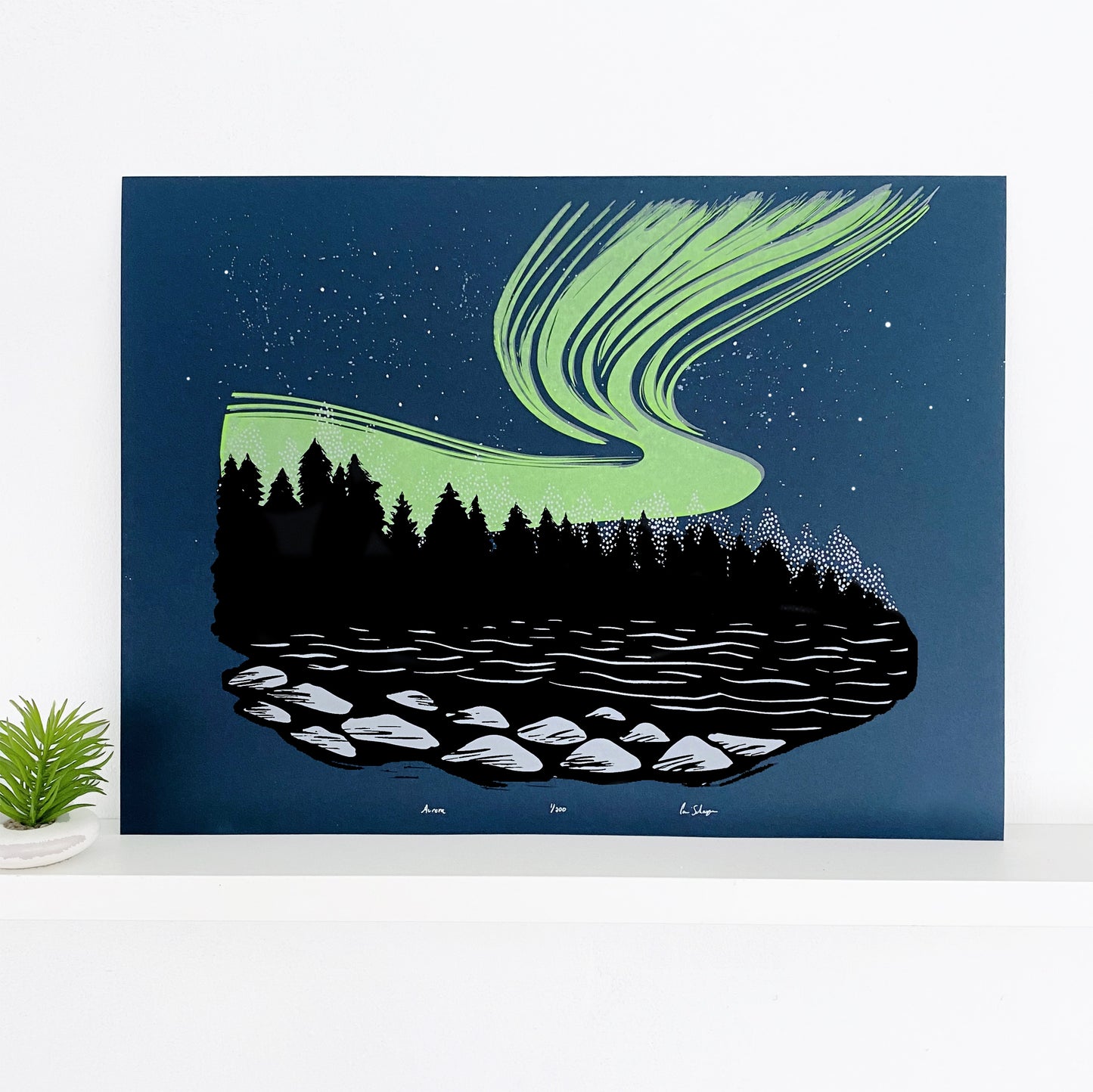 Northern lights artwork. A rich neon green aurora ink on top of a dark blue backround behind the shadows of a Black Forest. A lake in the foreground showing some light on rocks. Aurora Borealis front
